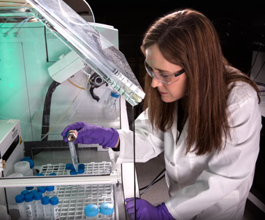 A scientist loads test tubes of samples into a mass spectrometer for forensic analysis.