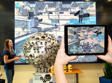 A computer tablet transforms a scale model of NIF's target chamber into augmented reality (AR) and VR views, which are also displayed on a giant video wall inside NIF's lobby.
