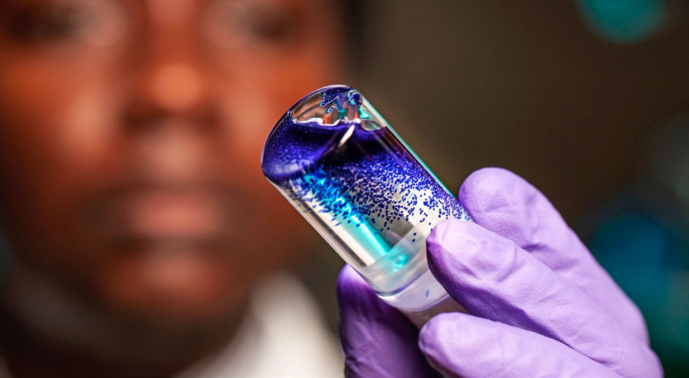 a scientist holding a vial of colorful liquid 
