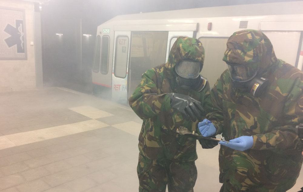 Two people wearing hazmat suits in front of subway car