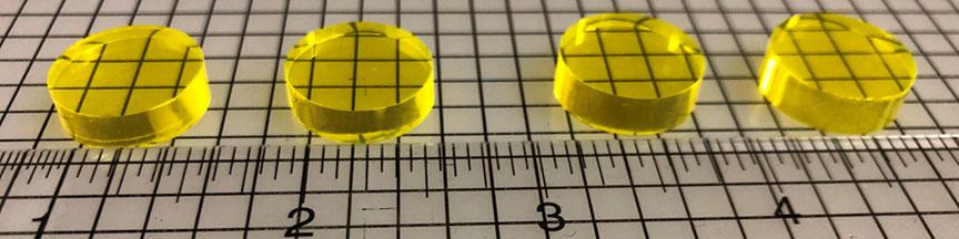 Four small, yellow, circular samples of transparent ceramic scintillators.