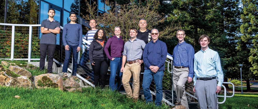 Ten scientists standing together on a hill outside a building.