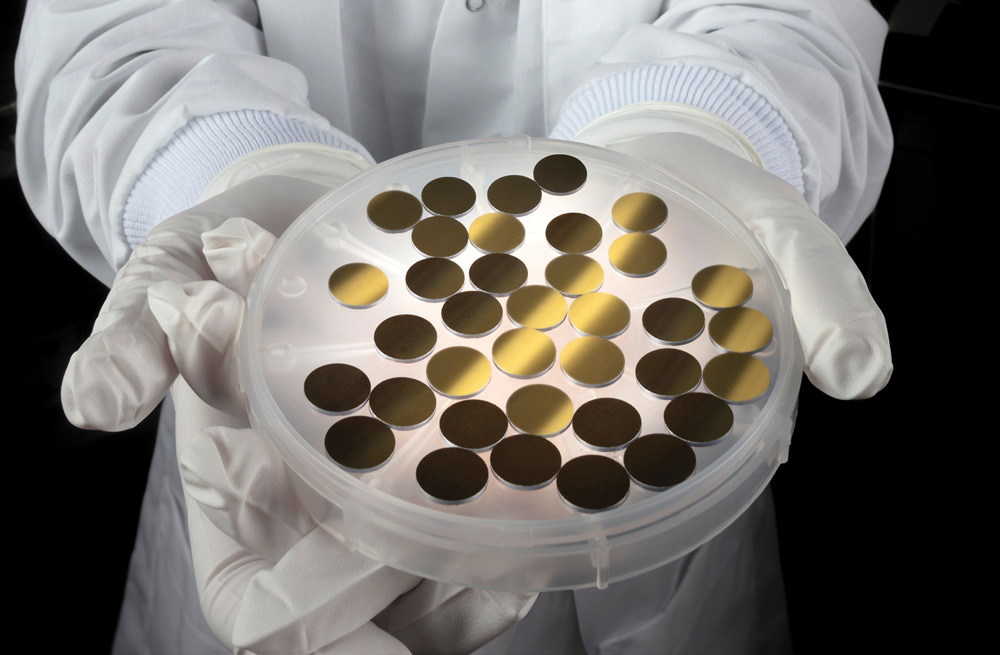 A woman in a lab coat holds a dish of gold discs.