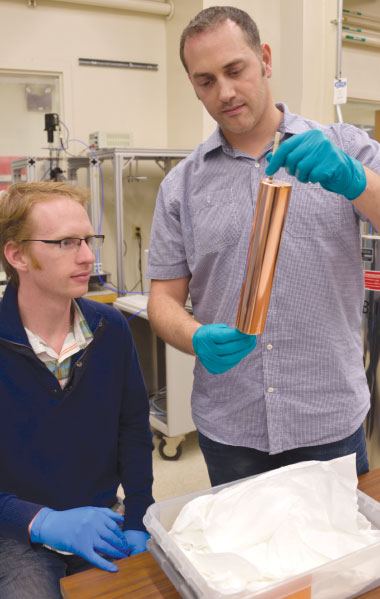 Physicist Gianpaolo Carosi (standing) and University of California at Berkeley student Jaben Root inspect a copper tuning rod for the Axion Dark Matter Experiment apparatus. This experiment uses a tunable resonant cavity immersed in a strong magnetic field to search for axion dark matter particles converting to detectable microwaves. (Photo by Alexandria Ballard.)